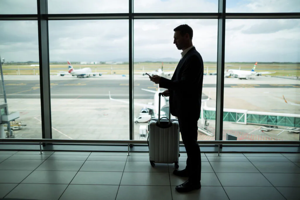 homem em pé no aeroporto mexendo no celular